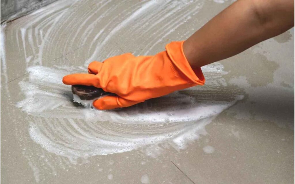 . A person with orange gloves actively cleaning a floor, showcasing a commitment to maintaining cleanliness.