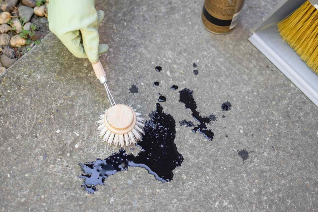Man Cleaning Set-In Hydraulic Oil Stain From Unsealed Concrete Floor Using Absorbent Material And Brush